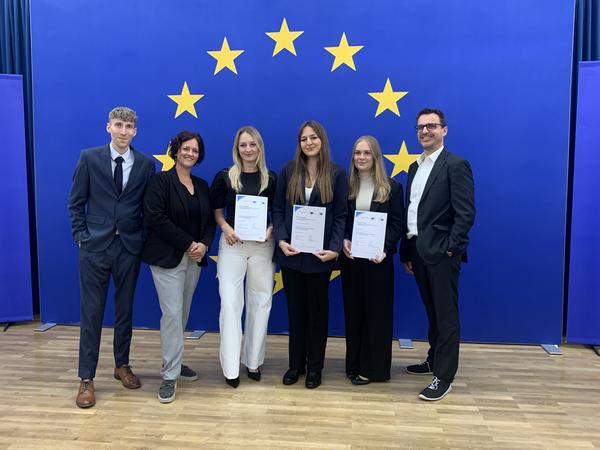 Fünf Personen mit Urkunden vor EU-Flagge, Europäische Union
