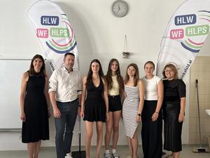 Schülerinnen der HLW Pinkafeld mit Lehrkräften und einem Vortragenden des Entrepreneurship Day zwischen zwei Beachflags der Schule
